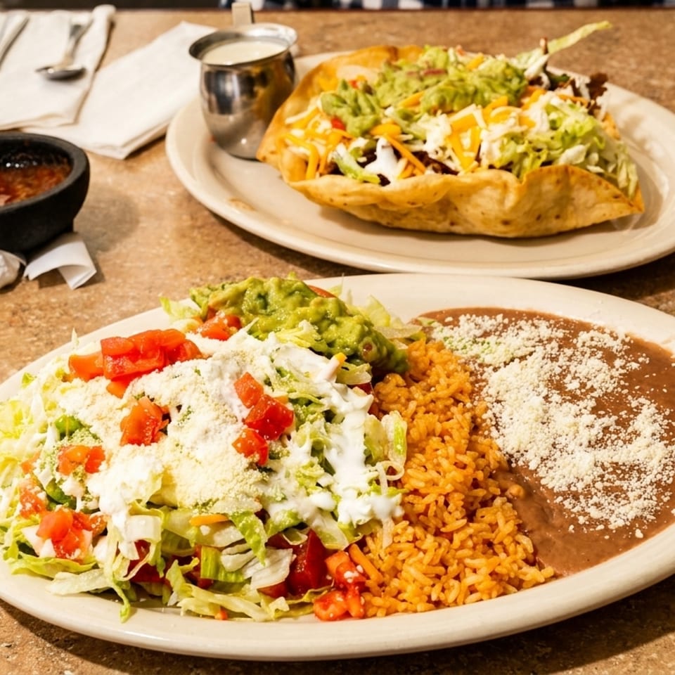Mexican meal with refried beans, rice, salad, guacamole, and a loaded taco served on a restaurant table.